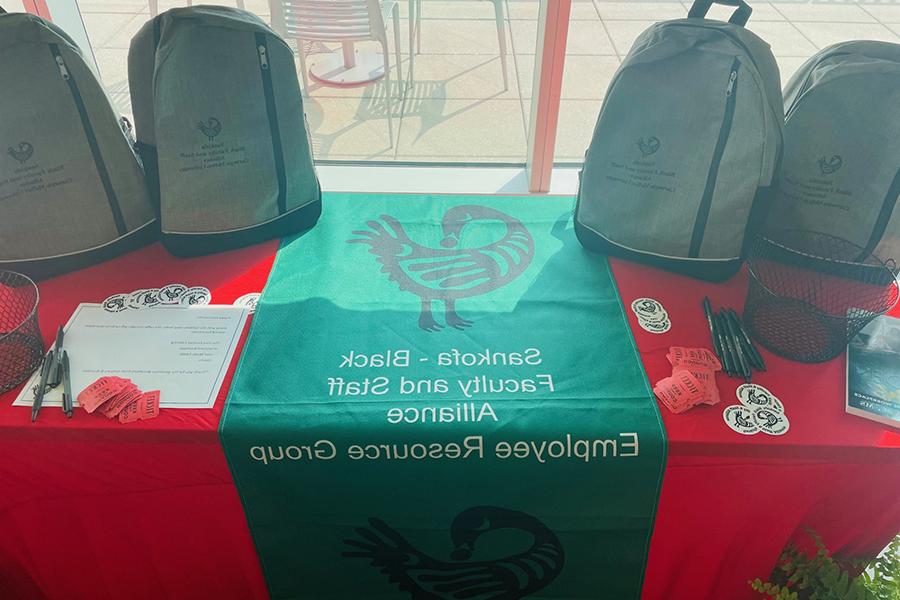 Table draped with Sankofa banner and handouts including stickers and backpacks